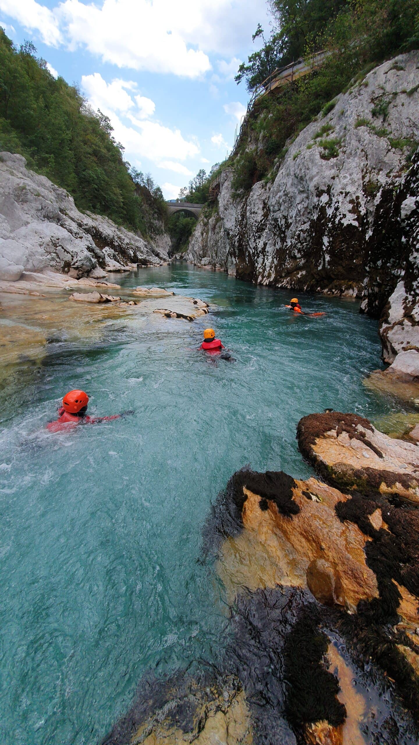 FAB Canyoning & Body Rafting Slovenia. Tres personas con chaleco y casco naranja practicando body rafting canyoning en un río celeste entre montañas en eslovenia